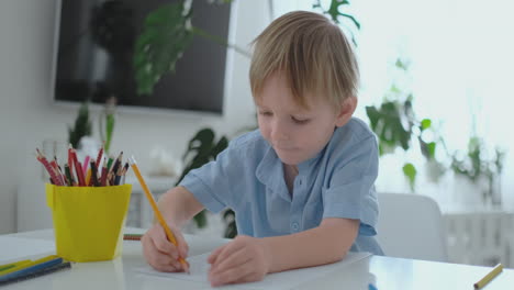 Un-Niño-Con-Una-Camiseta-Azul-Sentado-En-La-Cocina-En-La-Mesa-Dibuja-Un-Lápiz-Haciendo-La-Tarea-De-Entrenamiento-Preescolar